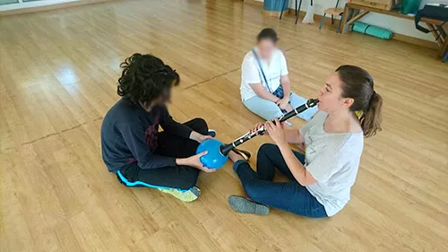 Tres personas sentadas en el suelo de un aula con un clarinete y cuencos sonoros en un taller de musicoterapia