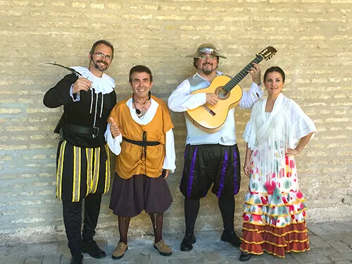 Grupo de actores con vestuario del Siglo de Oro y guitarra española ante un muro de ladrillo